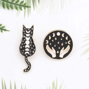 Black and gold enamel cat and lunar phase hand brooch pins set on white background