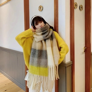 Close-up of thick beige and gray plaid scarf with soft tassels in a cozy indoor setting
