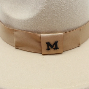 Close-up of beige wool fedora hat featuring a satin band and black metal M-logo detail