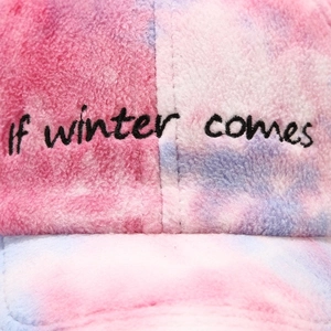 Close-up of tie-dye plush baseball cap with 'if winter comes' black embroidery detail
