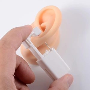 Manual ear piercing tool with white plastic shell and flesh-tone silicone ear mold