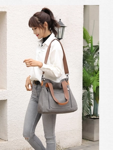 Outdoor shot of a grey canvas tote bag with brown straps worn by a model in casual style
