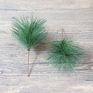 Close-up of 12cm artificial green pine needles on a light wood texture background