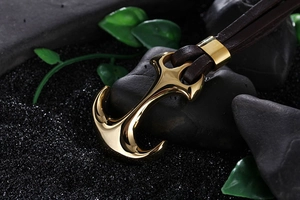 Macro shot of gold anchor pendant with dark brown braided leather strap on stones