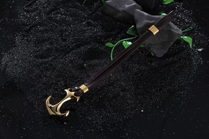Macro detail of golden anchor pendant on dark brown braided leather bracelet over black sand