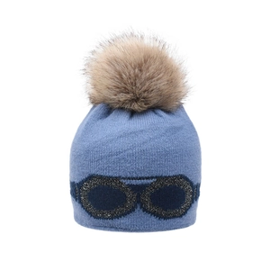 Close-up of blue knit hat with brown faux fur pompom and pilot goggles decoration
