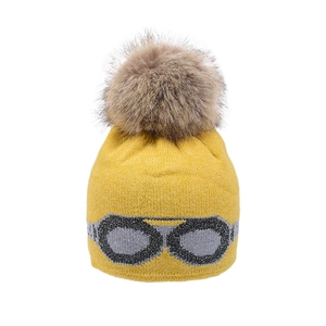 Detail of yellow knit beanie with faux fur pom and knitted goggle pattern