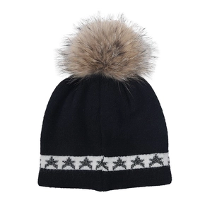 Détail du bonnet en maille noire avec motifs d'étoiles blanches et grand pompon marron doux