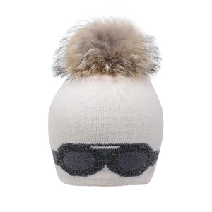 Détail d'un bonnet en maille crème avec pompon en fourrure et motif de lunettes