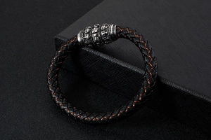 Macro detail of men's black braided leather bracelet with engraved skull metal clasp