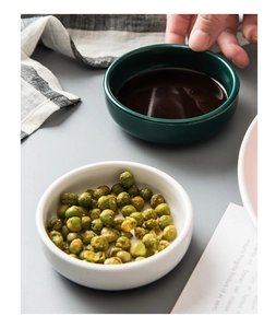 Close-up of ceramic dipping sauce dishes with green beans and dark soy sauce