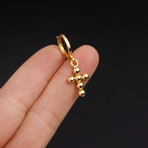 Detailed view of a gold cross earring made of small beads held against a black background