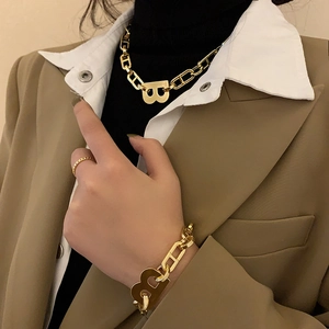 Detalle del conjunto de collar y pulsera con colgante B dorado y eslabones gruesos