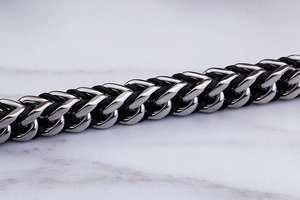 Detail of woven stainless steel chain with black leather inlay showing craft texture