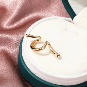 Macro shot of polished gold wavy metal ear cuff on a white velvet jewelry stand
