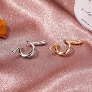 Punk style snake-shaped silver and gold cuff earrings on pink satin fabric background