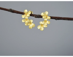 Artistic close-up of matte gold flower stud earrings hanging on a natural tree branch
