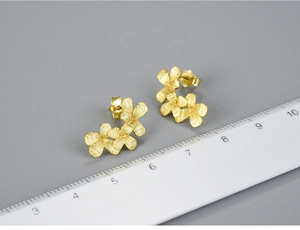 Macro shot of three-flower stud earrings in matte gold finish with ruler measurement