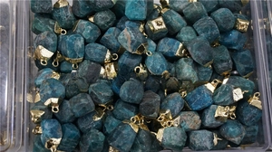 Bulk blue apatite raw stone pendants with gold plated edges inside a storage box