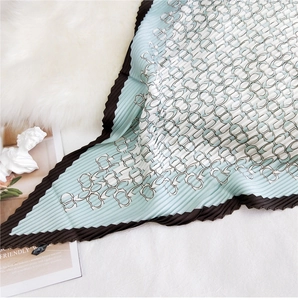 Macro detail of pleated silk scarf featuring mint green geometric patterns and brown borders
