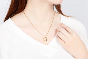 Close-up of a gold hollow heart pendant necklace worn by a model in a white top