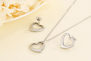 Detailed view of silver hollow heart necklace and earrings set on a beige background