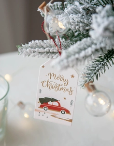 Close-up of a festive Christmas tag with a red vintage car hanging on a snowy pine branch
