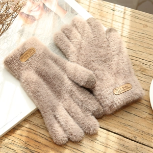 Detail of beige plush gloves featuring a small bear tag on a rustic wooden background