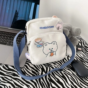 Close-up of white canvas crossbody bag featuring a cute bear print and blue strap