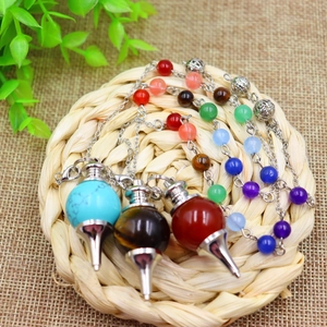 Detailed view of three natural 7-chakra stone pendulums on a rustic woven mat surface
