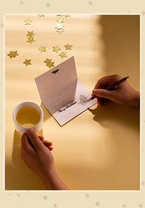 Person writing a Merry Christmas greeting card in a cozy setting with warm lighting