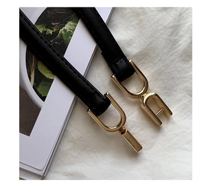Close-up of black faux leather belt with a distinctive gold metal arch-shaped buckle