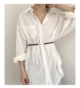 Detail of slim black waist belt with gold buckle styled over a long white shirt