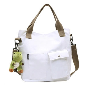 White canvas tote bag with brown straps and a green dinosaur plush charm, 45-degree view
