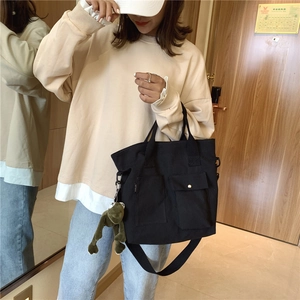 Detail of black canvas tote bag featuring external pockets and a plush frog pendant charm