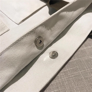 Detail of magnetic snap closure and durable white canvas texture on the tote bag