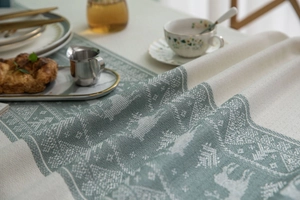 Detail showing the green and beige woven deer and tree pattern on the tablecloth fabric
