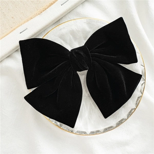 Elegant black velvet bow hair clip for women displayed on a white textured background