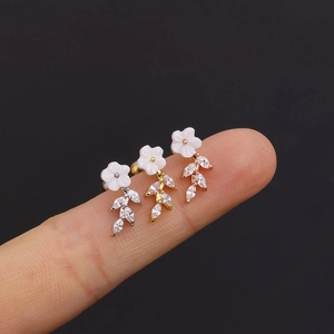 Macro view of dainty flower stud earrings in silver, gold, and rose gold on a finger