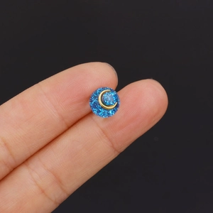 Blue glitter round mini stud earring with gold moon design on a polished resin surface