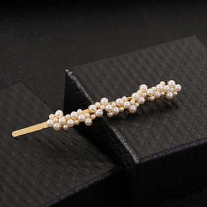 Barrette à cheveux dorée ornée de perles blanches sur un écrin de bijoux noir texturé