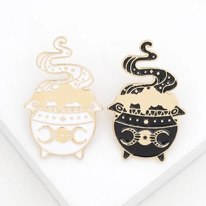 Detail of black and white enamel witch cauldron pins with mystical moon and star motifs