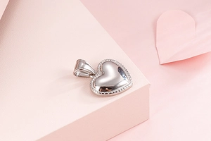 Detail of a polished silver heart pendant with textured edges on pink paper