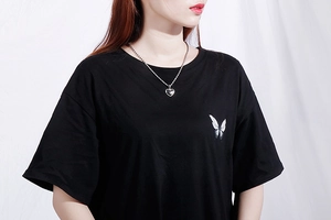 Close-up of a silver heart pendant necklace worn by a model in a black butterfly tee
