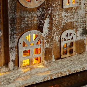 White wooden Christmas house with warm LED lights and glittery snow for festive decor