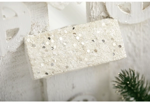 Close-up of white glitter surface on a wooden Christmas house ornament with pine needles