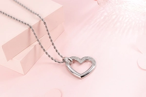 Détail macro du pendentif cœur argenté avec cristaux sur fond géométrique rose