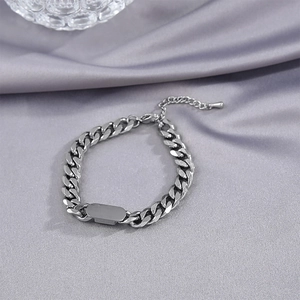 Close-up of a silver Cuban chain necklace with an engravable nameplate on silk fabric