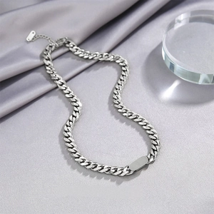 Close-up of silver Cuban chain necklace with rectangular nameplate on grey silk background