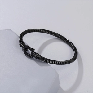 Macro shot of black twisted steel cable cuff with horseshoe buckle on grey pedestal